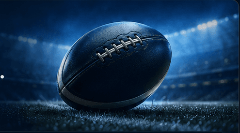 A rugby ball on the grass of a floodlit stadium.